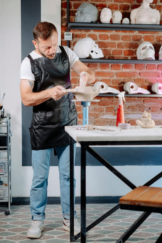 A man in an apron is making clay sculptures