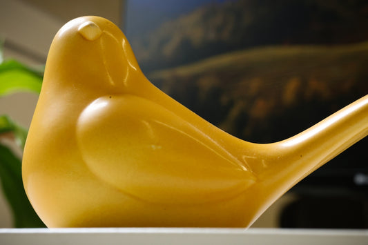 A yellow bird sculpture is displayed on a shelf.