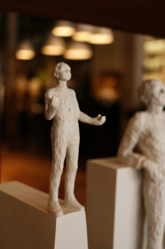 Two small sculptures stand on white pedestals.