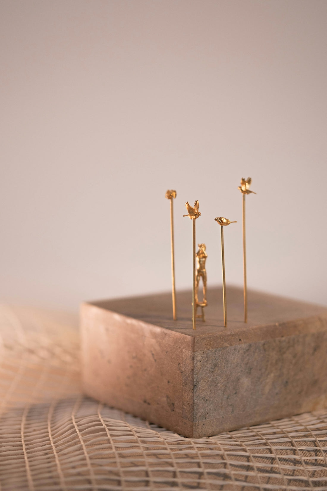 Delicate gold sculptures sit on a textured block.