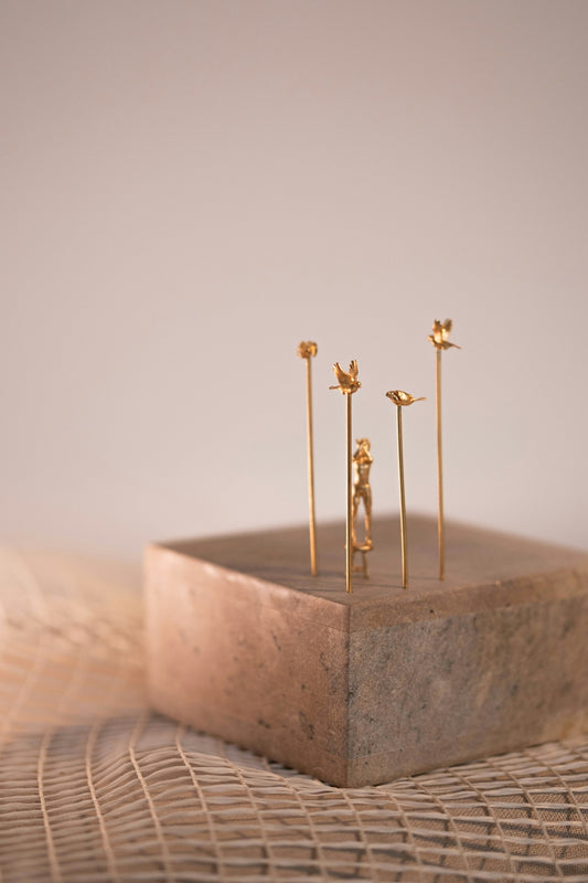 Delicate gold sculptures sit on a textured block.