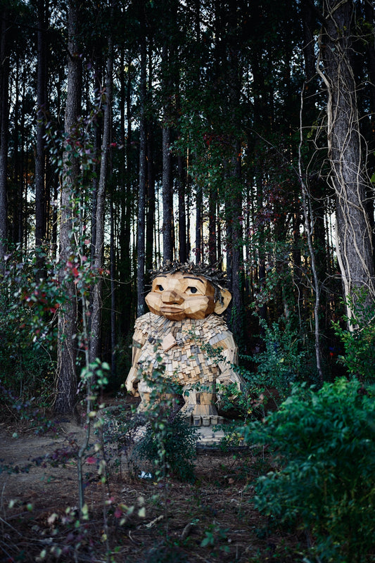 A wooden troll sculpture in a forest setting.